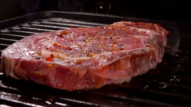 Baharatlı çiğ biftek ızgarada kızarıyor.