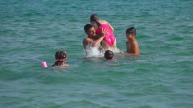 Bronzlaşmış genç adam çocukları deniz suyuna atıyor.