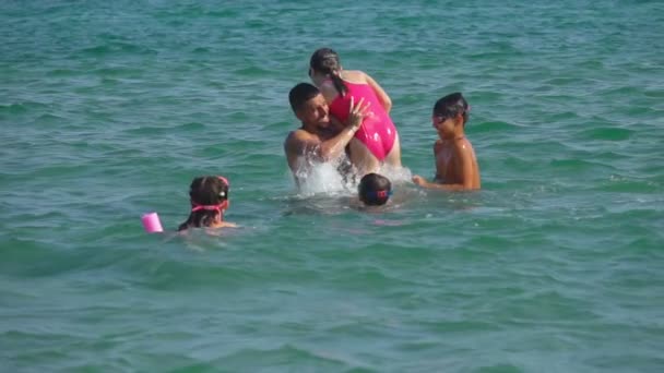 日焼けした若い男が子供たちを海の水に投げ込んでいる — ストック動画