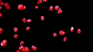 Olgun nar taneleri siyah arka planda çapraz olarak uçar.