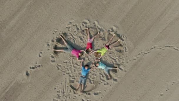 Gelukkige kinderen in heldere kleren liggen op het zand in de vorm van een ster — Stockvideo