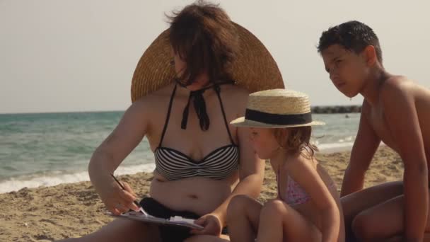 Junge Frau mit großem Hut zeigt Mädchen und Jungen, wie man Aquarellskizzen zeichnet — Stockvideo