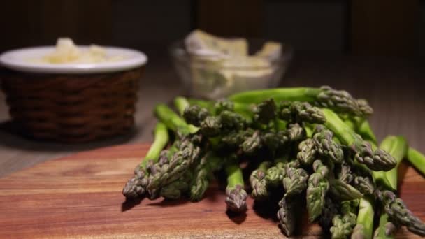 Lance sbucciate di asparagi verdi adagiate sulla tavola di legno accanto al formaggio blu — Video Stock