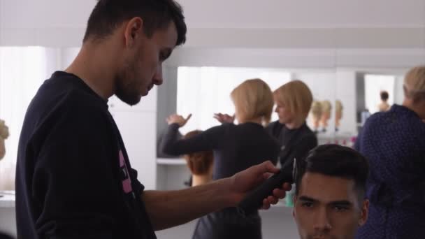 Estudante barbeiro está fazendo um corte de cabelo máquina sob a supervisão de um professor — Vídeo de Stock
