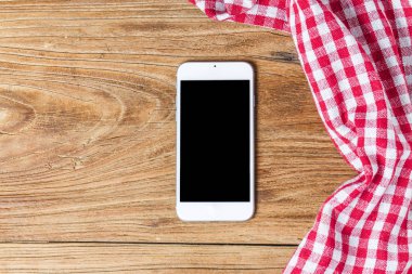 Boş ahşap masada cep telefonu ve kırmızı peçete.