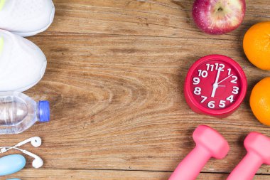 Dambılların, beyaz spor ayakkabıların, kırmızı saatin, akıllı telefonun, portakalların, elmanın, suyun ve kulaklıkların üst görüntüsü..