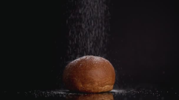 Polvilhe açúcar em pó no pão, câmera lenta no fundo escuro. Copyspace no topo — Vídeo de Stock