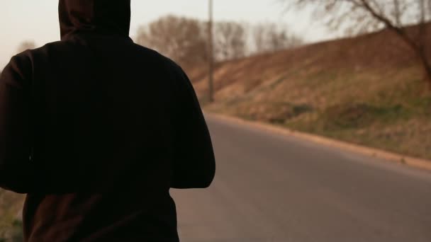 Одинокий бегун на закате на улице в черном свитере в капюшоне. Медленное движение — стоковое видео