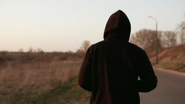 Lone runner o zachodzie słońca na zewnątrz w czarny sweter z kapturem. Zwolnionym tempie — Wideo stockowe