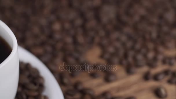 Caffè in tazza bianca circondato da chicchi di caffè su sfondo scuro in 4k UHD — Video Stock