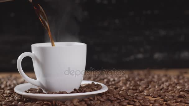 어두운 배경에 커피 콩으로 둘러싸인 흰색 컵에 커피를 따르고. 4 k — 비디오