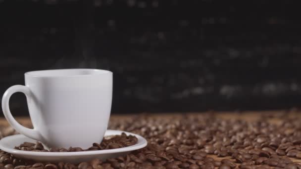 Café en taza blanca rodeado de granos de café sobre fondo oscuro en 4k UHD — Vídeo de stock