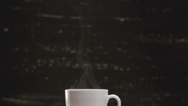 Koffie in witte kop, omringd door de koffiebonen op donkere achtergrond in 4k Uhd — Stockvideo