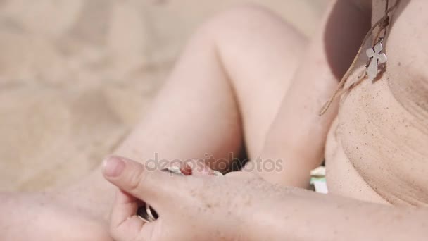Маленька мила дівчинка грає з піском і черепашками на пляжі. Крупним планом 4k — стокове відео