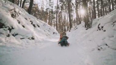 Genç anne ve küçük kızı slomo içinde kış Park kızak üzerinde eğleniyor