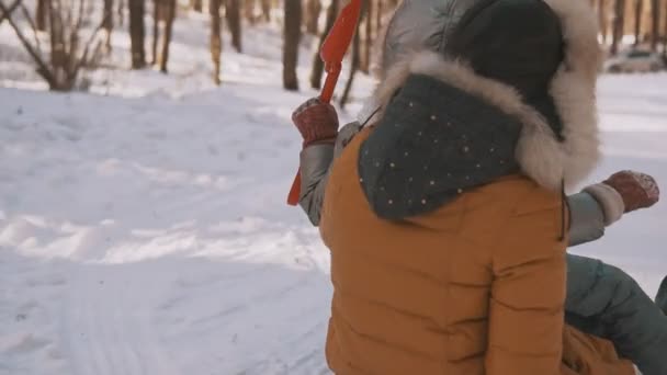Молода мати і маленька дочка розважаються на санях в зимовому парку — стокове відео
