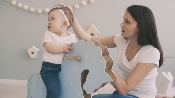 Jovem mãe e filha se divertindo com cavalo de brinquedo em câmera lenta interior — Vídeo de Stock