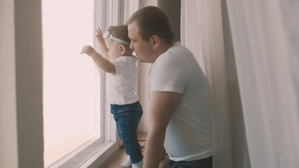 Junger Vater steht mit seiner süßen Tochter am Fenster im Slomo — Stockvideo