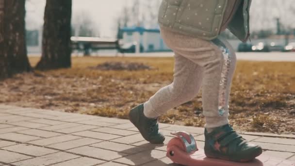 Kleines Mädchen fährt mit rosafarbenem Roller auf Bürgersteig in Slomo — Stockvideo