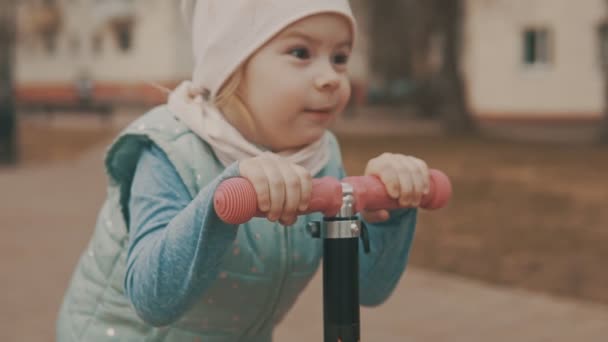 Kleines Mädchen fährt in Zeitlupe auf rosa Roller auf Bürgersteig — Stockvideo