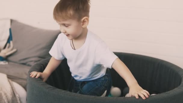 Маленький хлопчик грає в басейні кольорових кульок — стокове відео