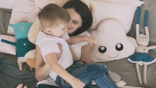 Молодая мать и маленький сын веселятся в спальне в замедленной съемке — стоковое видео