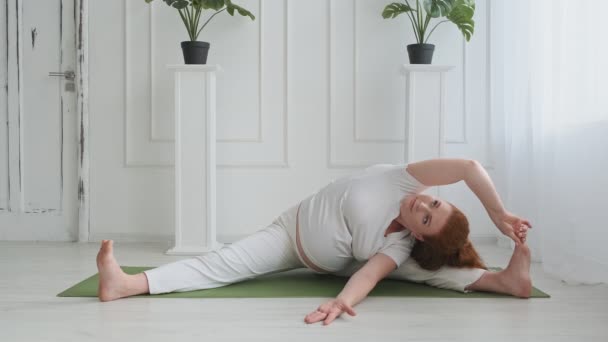 Vacker gravid kvinna som gör yoga på golvet. Ung hona som sträcker sig inomhus. — Stockvideo