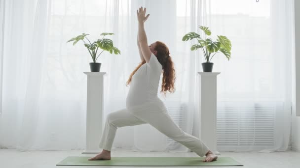 Zwangere vrouw die yoga doet en binnenshuis in een krijgerspositie staat. Actief zwanger. — Stockvideo
