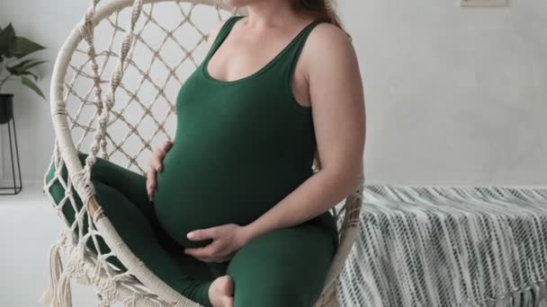 Beautiful redhead pregnant woman sitting in hanging chair and touching belly — Stock Video