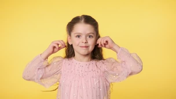 Caucasian kid girl in pink dress doing silly funny face at yellow background. Portrait of cute little girl playfully making faces looking at camera. Positive emotion. Medium shot in 4k, UHD — Stock Footage Caucasian Kid Girl Pink Dress Doing Silly Funny Face Yellow Stock Video