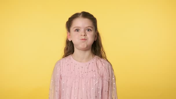 有趣的小女孩在镜头前开玩笑地做鬼脸 积极的情绪 穿着粉红衣服的白人小女孩做着傻傻的滑稽脸 在黄色背景下鼓起双颊 中弹4K Uhd — 图库视频影像
