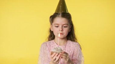 Küçük üzgün kız sarı arka planda doğum günü pastasında mum üflüyor. Pembe elbiseli beyaz bir kızın yakın plan portresi. Yalnızlık kavramı. 4k, Uhd