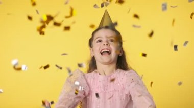 Konfeti atan mutlu küçük kız. Pembe elbiseli ve parti şapkalı neşeli çocuk. Bayram ve parti kavramı ağır çekimde. Pozitif duygular.