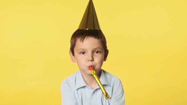 兴奋的男孩把金发碧眼的圆饼抛向空中 假日和聚会的概念 快乐的小男孩穿着蓝色的衬衫 背景是黄色的 慢动作 — 图库视频影像
