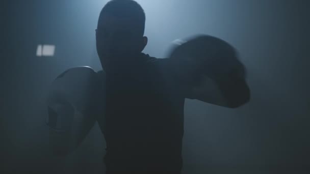 Boxer behúz a kamerába. Fiatal bokszoló sziluettje, aki bokszütéseket gyakorol — Stock videók