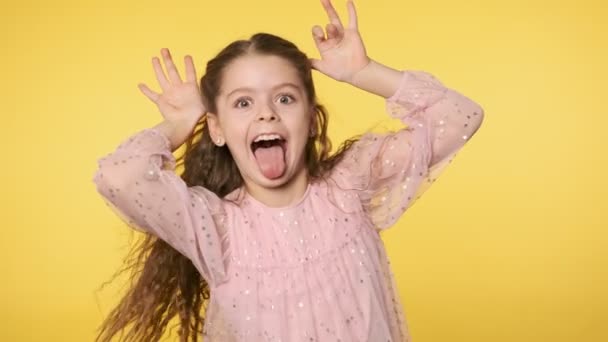 Funny little girl making silly faces looking at camera. Girl in pink dress sticking her tongue at yellow background in slow motion. 4k, UHD 60FPS slow motion — Stock Footage Funny Little Girl Making Silly Faces Looking Camera Girl Pink Royalty Free Stock Video