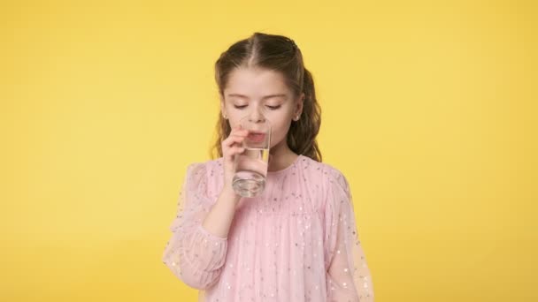 水のガラスと子供のクローズアップ肖像画 黄色の背景のガラスからきれいな水を飲む美しい子供の女の子 スローモーション Uhd — ストック動画