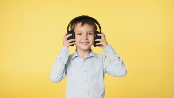 穿着蓝色衬衫的小男孩在耳机里听音乐 在黄色背景下跳舞 演播室里的漂亮男人 Uhd — 图库视频影像