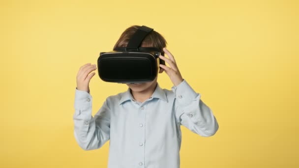 Маленький мальчик в наушниках виртуальной реальности стоит в студии и смотрит вокруг — стоковое видео