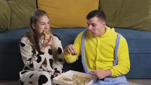 Ευτυχισμένο ζευγάρι με αστείες πιτζάμες που τρώει φαστ φουντ. Ζευγάρι χαλαρώνοντας και τρώγοντας πίτσα — Αρχείο Βίντεο
