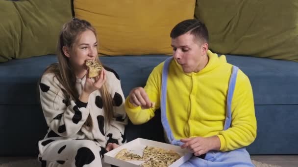 Pareja feliz en pijamas divertidos comiendo comida rápida. Pareja relajante y comer pizza — Vídeo de stock