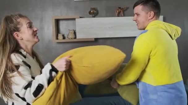 Jovem casal de pijama jogando travesseiro luta no quarto. Família em kigurumi — Vídeo de Stock