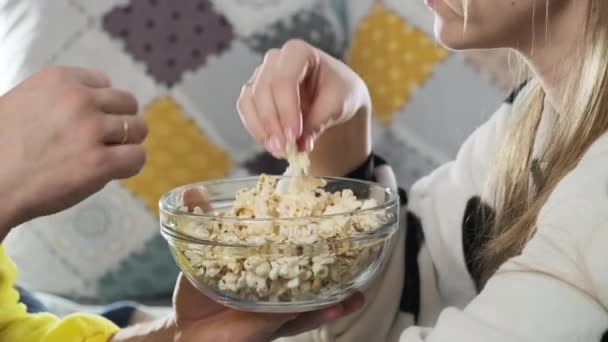Couple in pajamas sitting on sofa with pop corn. Close-up view of hands — Stock Video