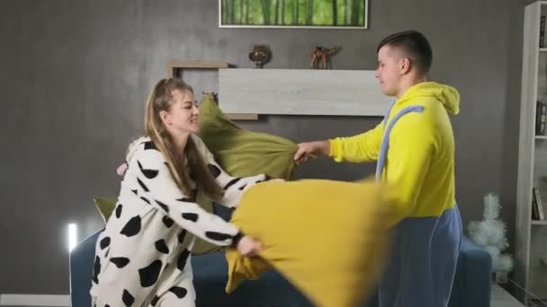 Młoda para w piżamie bawiąca się w walkę na poduszki w sypialni. Walki rodzinne — Wideo stockowe