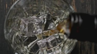 Kahverengi şişeden bardağa viski döküldü. Üst Manzara. Buzlu viski bardağının yakın çekimi. Viskiyi yavaş çekimde dolduruyorum.