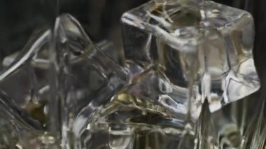Ağır çekimde buz küpleriyle bardağa dökülen viski makrosu. Şişeden bardağa alkol dökülüyor.