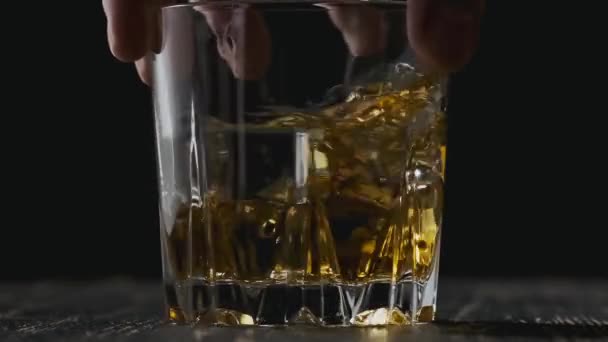 Mann hält Glas mit Whiskey in der Hand. Glas mit Whiskey rotiert am Holztisch. — Stockvideo