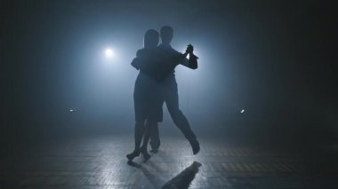 Kadın ve erkek dumanlı baloda tango yaparken profesyonel hareketler yapıyorlar.