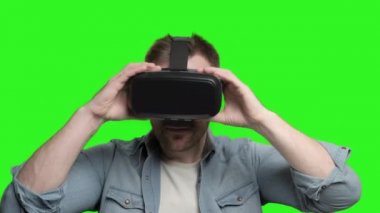 Young man on green chroma putting on VR glasses and looking around. Cheerful guy