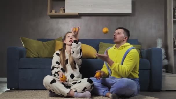 Pareja Pijama Kigurumi Divirtiéndose Sala Estar Haciendo Malabares Con Mandarinas — Vídeo de stock